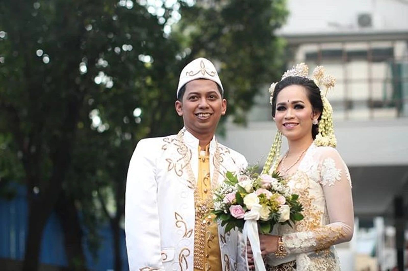 Pasangan pengantin memakai busana akad putih dengan aksen emas