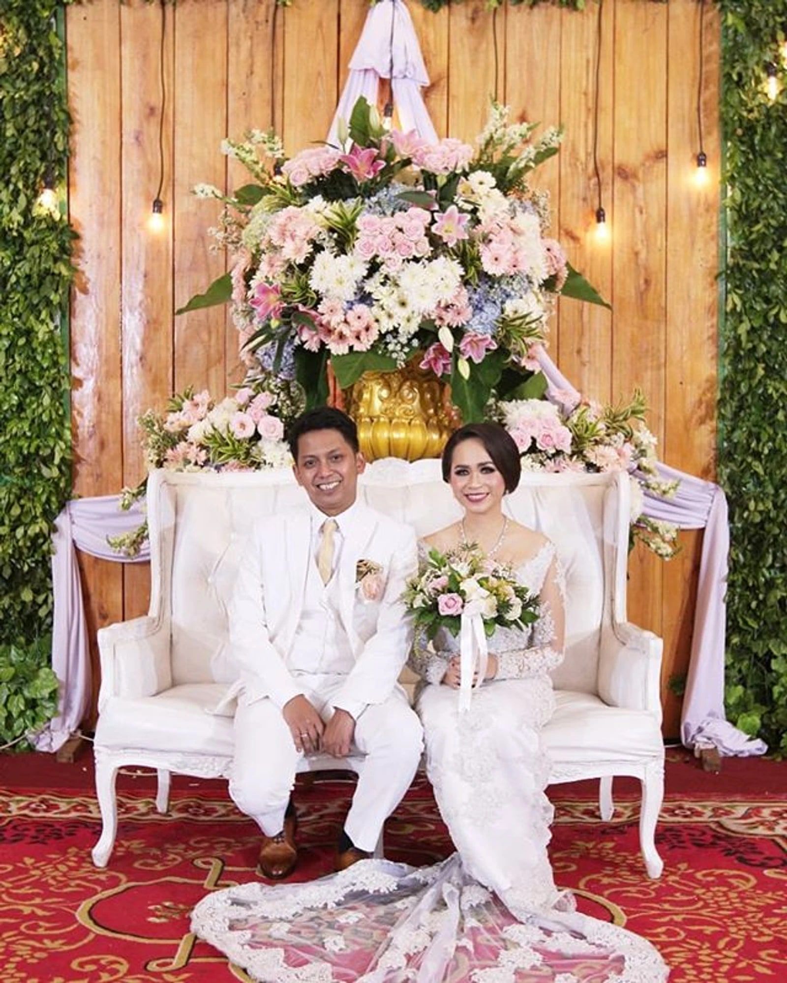 Pasangan pengantin duduk di pelaminan berhias bunga pastel