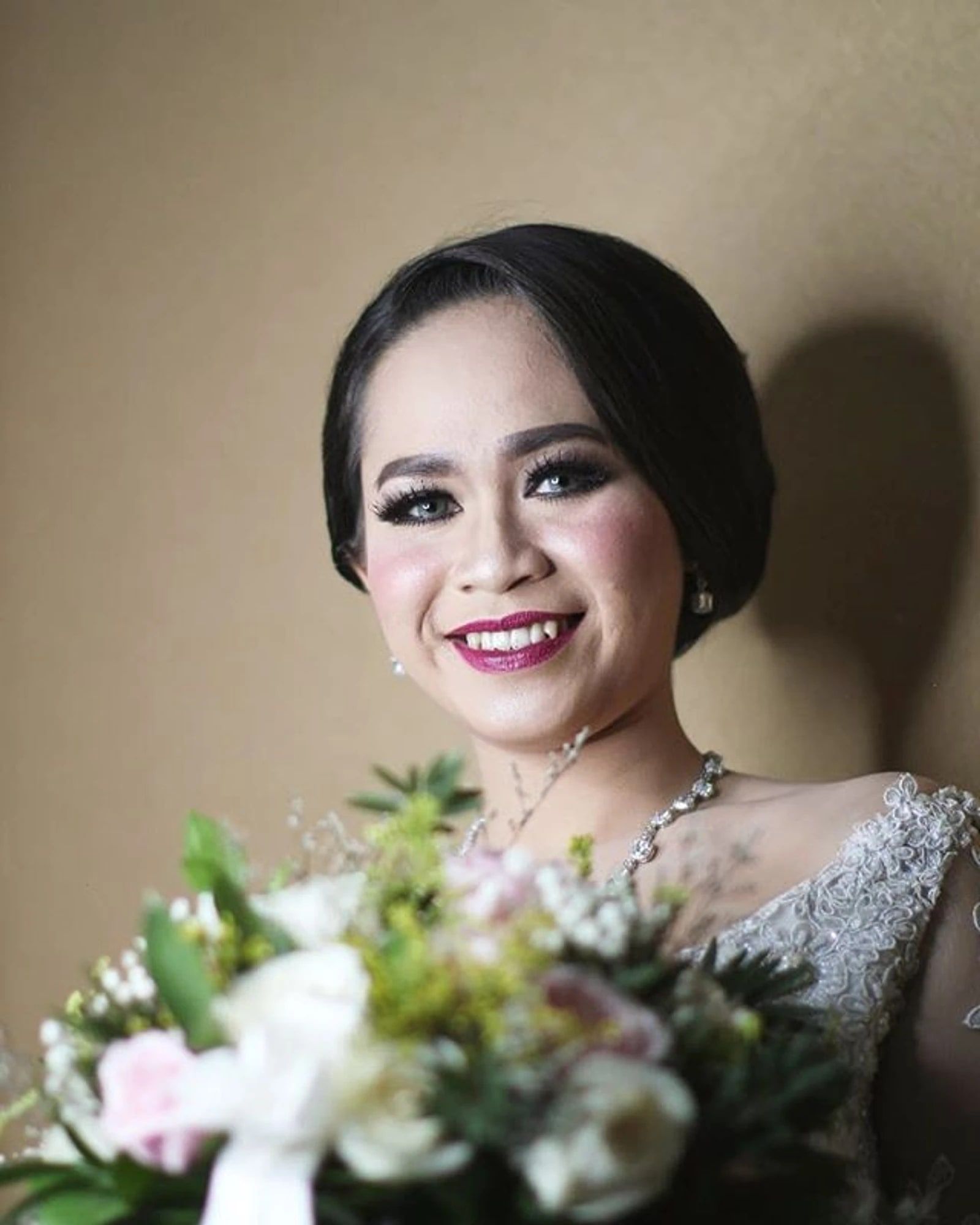 Potret pengantin wanita tersenyum dengan riasan bold dan buket bunga