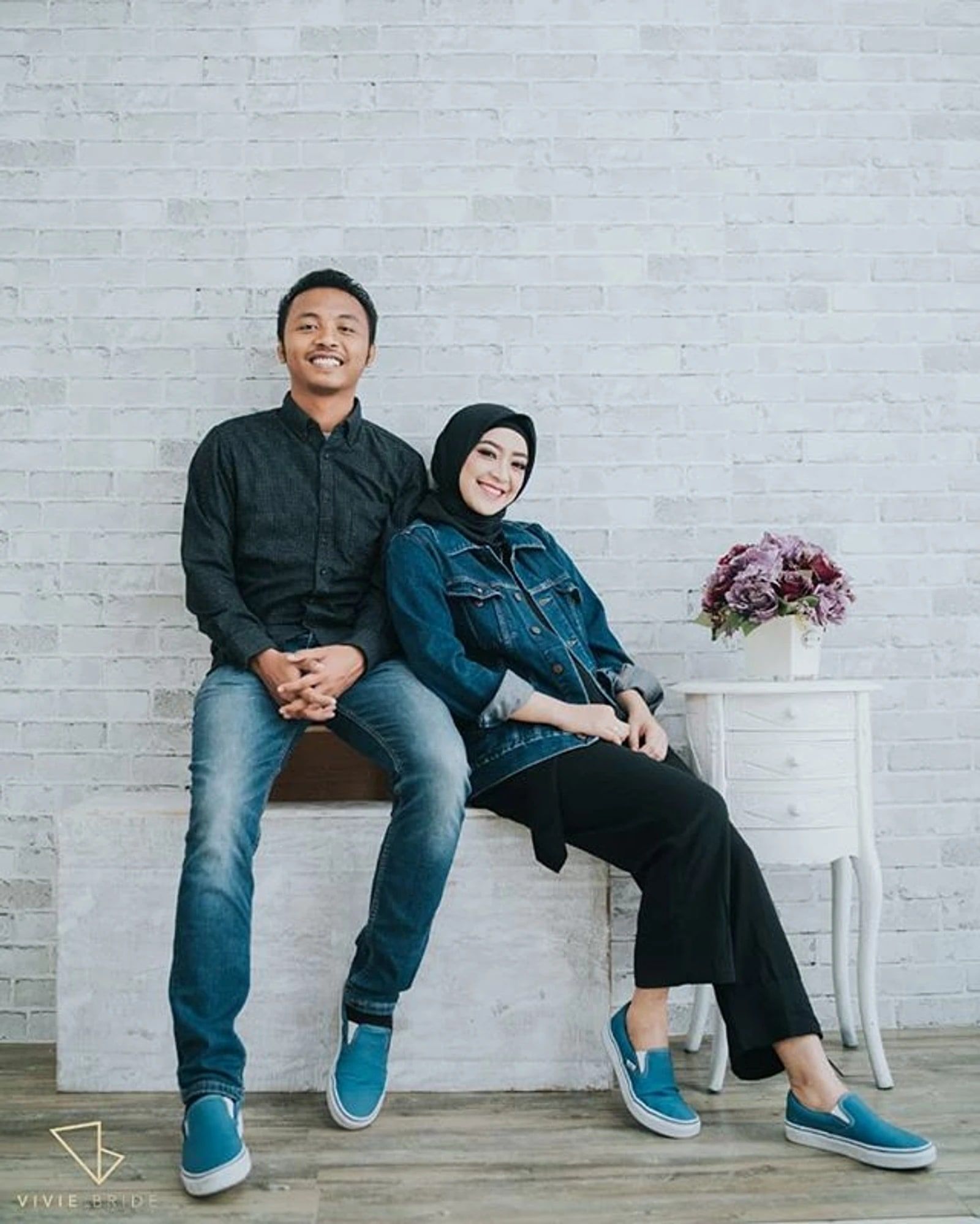 Pasangan prewedding duduk bersandar di studio berdinding bata putih