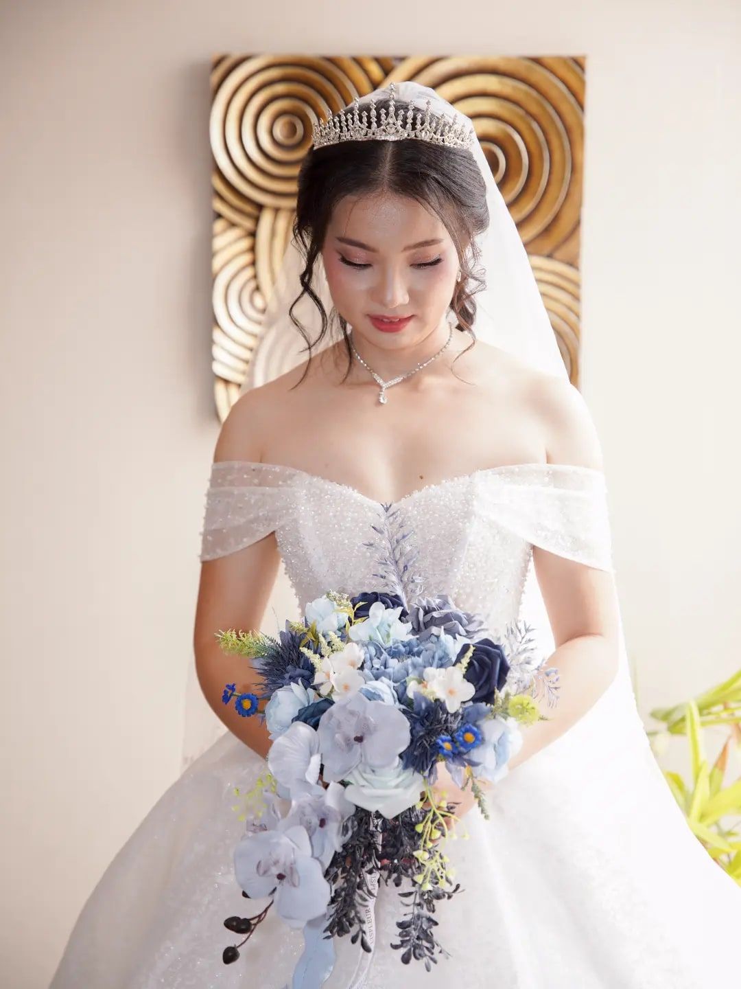 Pengantin wanita dengan tiara, gaun off-shoulder, dan buket biru putih