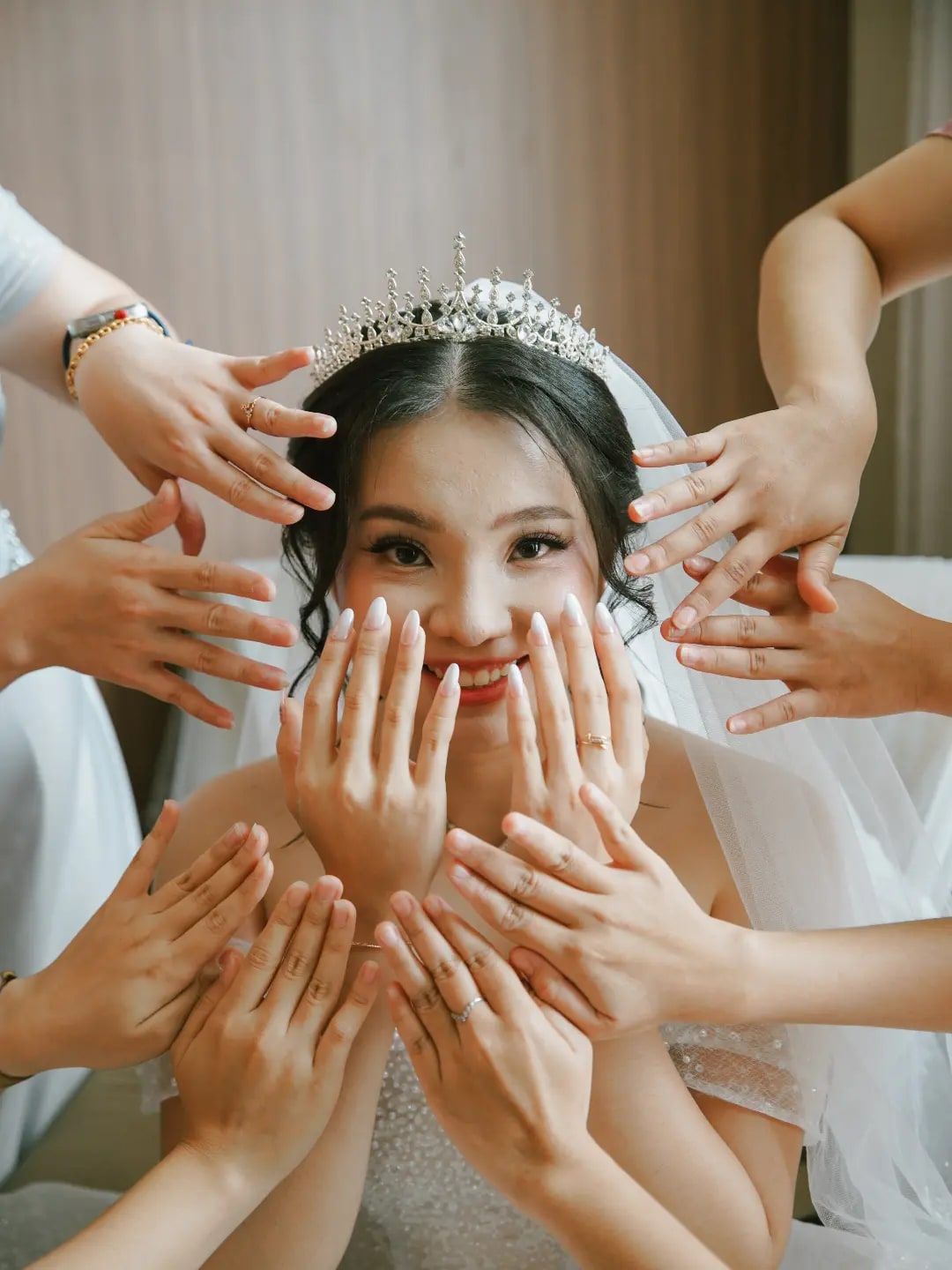 Pengantin wanita bertiara tersenyum dikelilingi tangan para bridesmaid