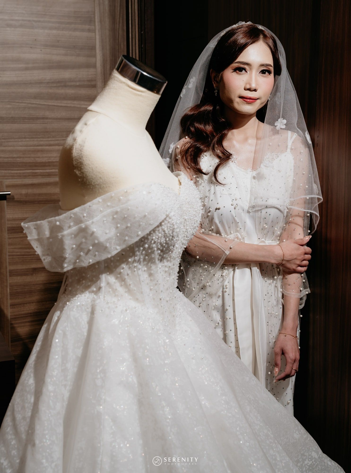 Pengantin wanita berdiri di balik gaun ball gown pada manekin, menatap ke kamera